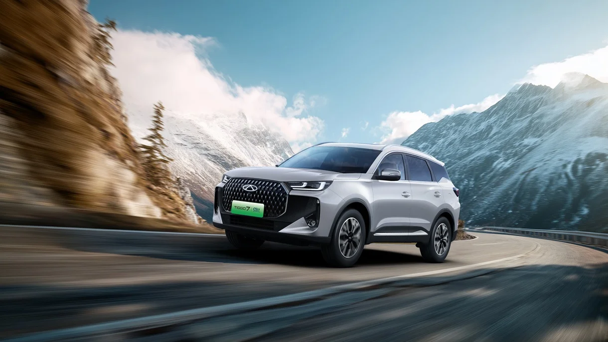Grauer TIGGO 7 SUV auf einer Landstraße, fährt in einer Kurve, im Hintergrund Berge zu sehen